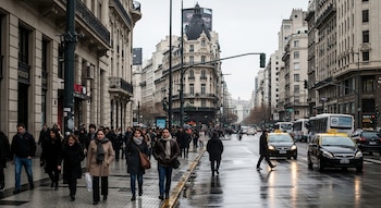 Rua com pessoas andando, carros, táxis, ônibus, edifícios históricos, semáforos e postes de luz sob o céu branco.