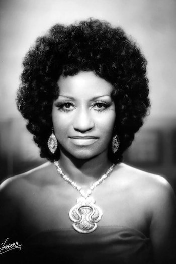 Fotografía en blanco y negro del busto de una mujer con peinado afro, aretes colgantes y un collar con colgante grande