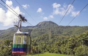 Un teleférico amarillo, verde, azul y rojo con el número "1" subiendo por cables sobre un paisaje montañoso cubierto de densa vegetación bajo un cielo azul