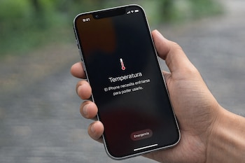 Primer plano de una mano sosteniendo un iPhone con la pantalla en negro mostrando un mensaje de advertencia de 'Temperatura' y un icono de termómetro rojo.