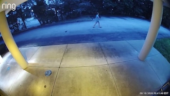 Una persona camina por un camino pavimentado visto desde el pórtico con columnas de una casa