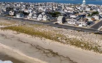 Vista aérea de un suburbio costero con numerosas casas de distintos colores, una carretera, dunas de arena, una playa y el océano