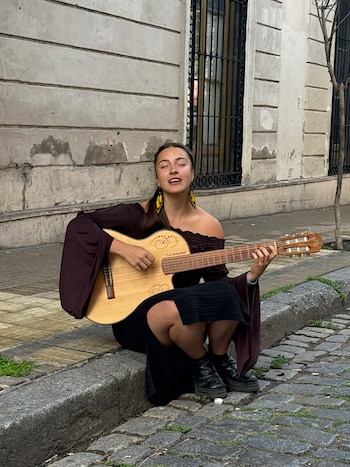 Una persona con cabello largo toca una guitarra acústica con los ojos cerrados frente a un micrófono en un escenario iluminado