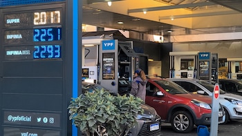 Estación de servicio YPF con cartel digital de precios de combustibles Super, Infinia e Infinia Diesel. Una persona atiende un surtidor, varios coches están estacionados