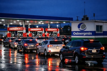 Amplia estación de servicio al anochecer con largas filas de coches esperando. Surtidores muestran carteles rojos de 'EMERGENCIA'. Un letrero de Osinergmin se ve en la caseta de control.