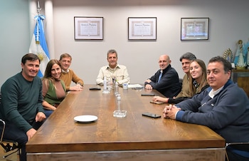 Ocho personas (cinco hombres, tres mujeres) sentadas alrededor de una mesa de madera oscura en una sala de reuniones. En el fondo, una bandera argentina y cuadros en la pared