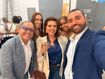 Selfie de cinco personas sonrientes, incluyendo a William Meléndez García con gafas, Alicia Machado en blazer crema, y Carlos Mesber con barba