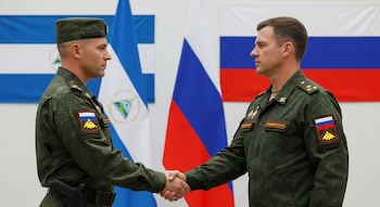 Dos soldados, uno nicaragüense y otro ruso, se estrechan la mano con seriedad. Visten uniformes militares verdes. Detrás, las banderas de Nicaragua y Rusia ondean.