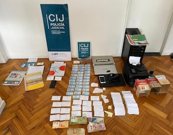 Objetos incautados por la Policía Judicial CIJ exhibidos en un suelo de madera, incluyendo laptops, teléfonos, impresora, dinero en efectivo, documentos de identidad y otros papeles