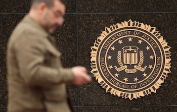 Un sello circular dorado con el texto 'FEDERAL BUREAU OF INVESTIGATION DEPARTMENT OF JUSTICE' en una pared oscura, con una figura humana borrosa pasando por delante