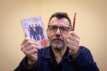 Hombre con barba y gafas sostiene en una mano el libro 'Tinta Roja' de Alberto Fuguet y en la otra una pluma roja