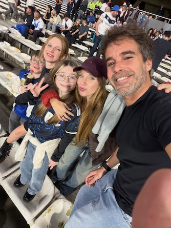 Fotografía en primer plano tomada por un hombre junto a una mujer con gorra y dos niños en las gradas de un estadio