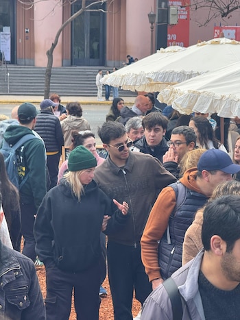 Un hombre con anteojos de sol y una mujer con gorro verde caminan tomados del brazo entre una multitud al aire libre