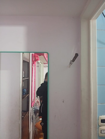 Un cuchillo con mango oscuro y hoja plateada está incrustado en una pared clara. Un espejo a la izquierda refleja el torso de una persona y un objeto naranja