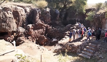 Un grupo de personas permanece junto a una excavación rocosa al aire libre con formaciones de piedra y vegetación