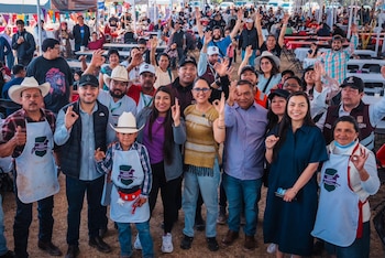 Gran multitud de personas sonrientes en un evento al aire libre. Muchos hacen gestos de aprobación o saludan, algunos con delantales de la Expo Barbacoa Tlaxcala