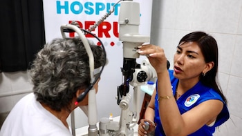 Una médica con uniforme azul utiliza una lámpara de hendidura para revisar el ojo de una paciente sentada frente al aparato