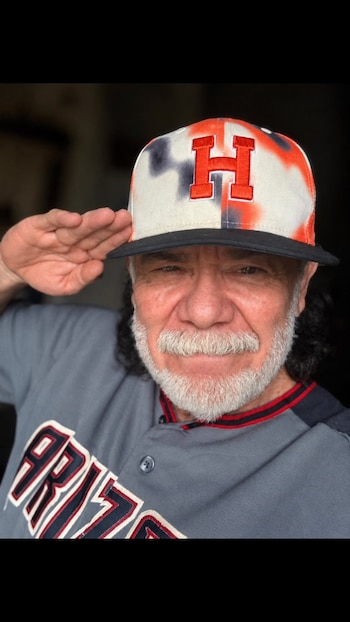 Primer plano de un hombre con barba blanca y gorra que realiza un saludo con la mano derecha levantada a la altura de la sien