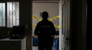 Oficial de policía de espaldas en la entrada de una habitación acordonada con cinta amarilla de "POLICIAE", observando el interior. Equipo forense visible a la izquierda.