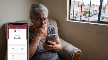 Mujer adulta mayor sentada en un sillón, sosteniendo un teléfono móvil con la pantalla que muestra un saldo de 0.00 de Pensión Mujeres Bienestar.