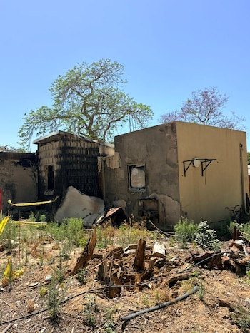 Vista exterior de una casa parcialmente destruida por un incendio, con paredes ennegrecidas, escombros en el suelo y vegetación seca