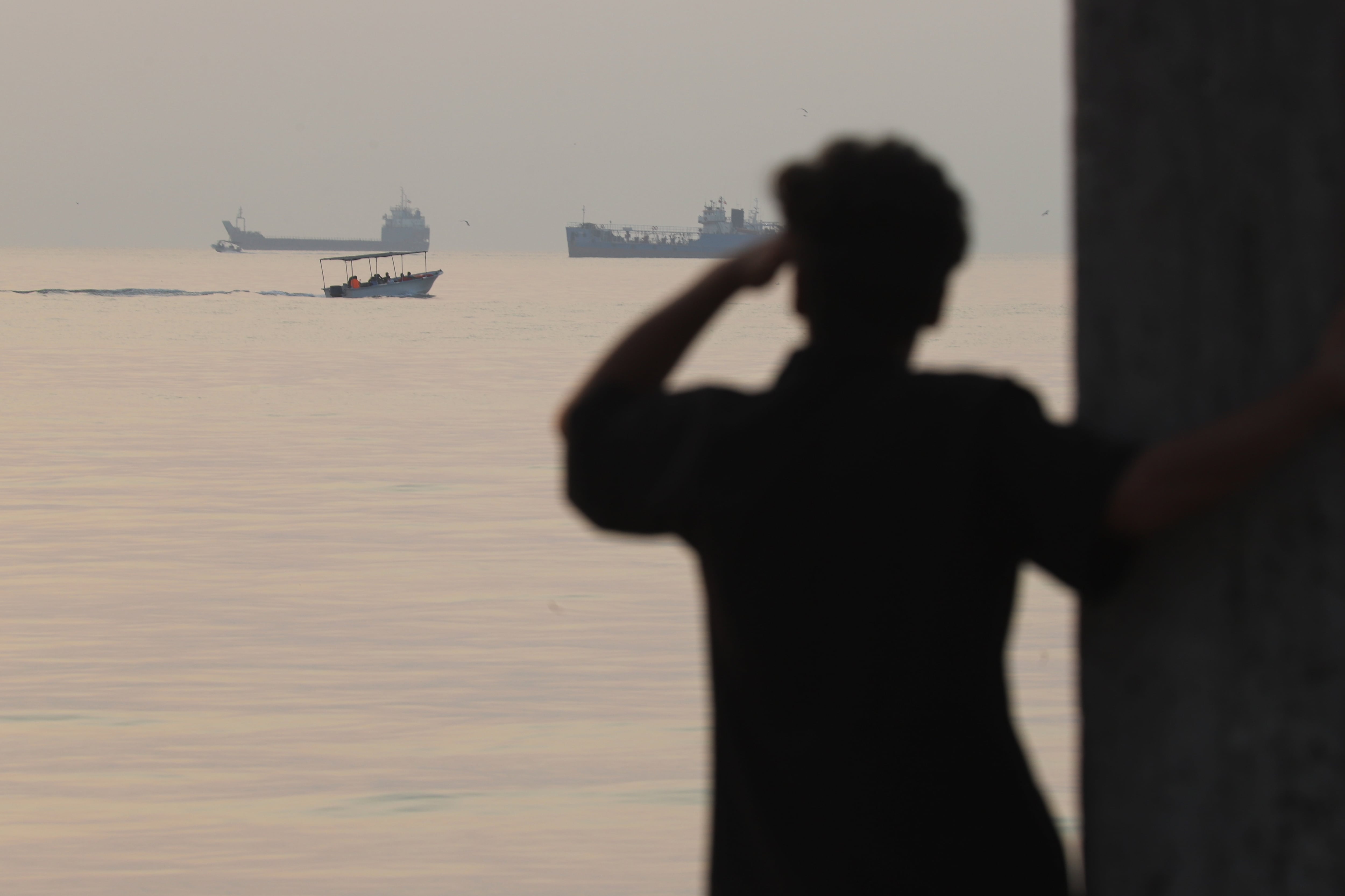 Un hombre observa el mar mientras una pequeña embarcación pasa frente a buques de carga anclados en el estrecho de Ormuz, el sábado 24 de octubre de 2026, en Bandar Abbas, Irán. (Amirhosein Khorgooi/ISNA via AP)