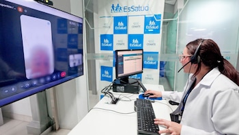 Una mujer con bata blanca y auriculares atiende dos monitores de computadora. Uno muestra una videollamada y otro una interfaz de datos. Fondos con logos de EsSalud y CENATE