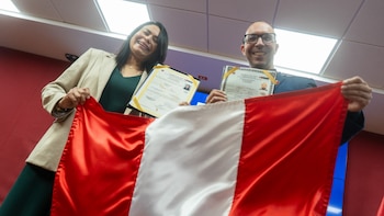 Una mujer y un hombre sostienen una bandera peruana roja y blanca mientras muestran carpetas con sus documentos oficiales