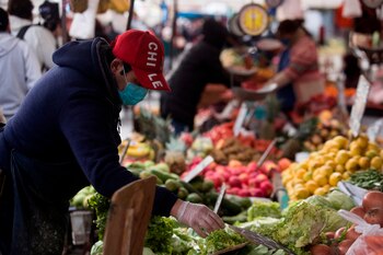 Un vendedor trabaja el pasado martes 8 de julio en la feria libre de la comuna de Peñalolén en Santiago (Chile). Olaya rocía con alcohol las monedas que acaba de darle un cliente y luego se embadurna bien las manos. EFE/Alberto Valdés