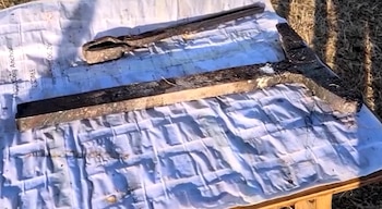 Tenazas de hierro y una estructura en forma de T colocadas sobre un papel con diagramas impresos sobre una superficie de madera