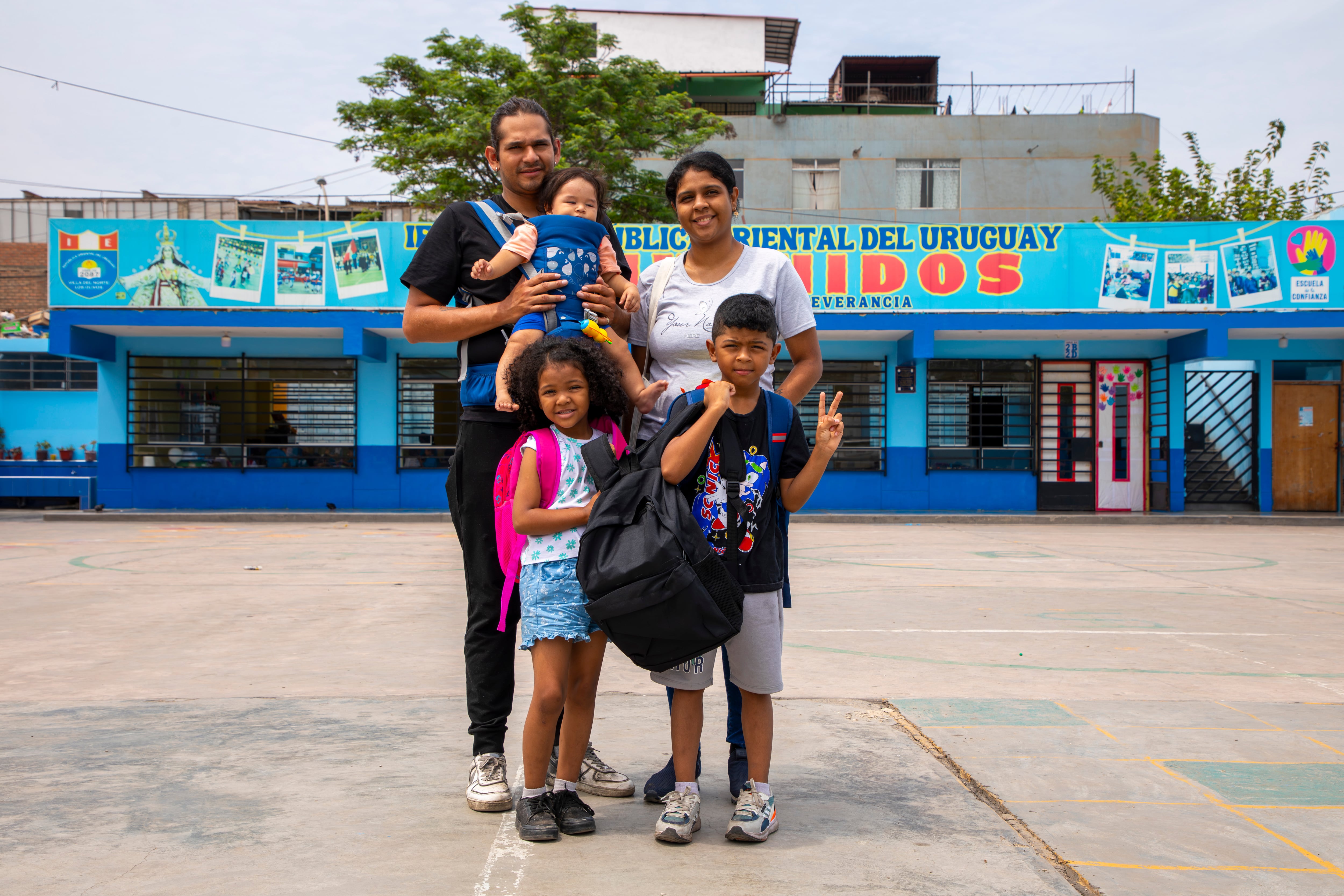 Una familia sonriente, posiblemente beneficiaria de ACNUR, posa frente a un edificio azul con un cartel que dice