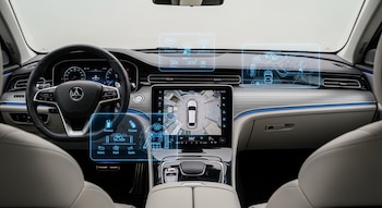 Interior de un sedán de lujo con volante, panel digital de instrumentos, pantalla central con vista 360 del vehículo y gráficos holográficos flotantes.