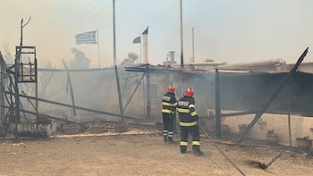 Los bomberos intentan extinguir un incendio en un edificio en llamas, mientras un incendio forestal arde en la isla de Rodas, Grecia