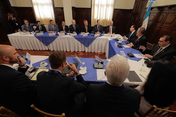 Un grupo de hombres con traje formal está sentado alrededor de una mesa en forma de U con las banderas de Guatemala y Estados Unidos