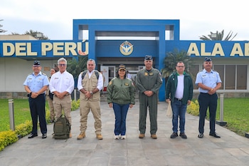 Siete personas, incluyendo militares y civiles, posan frente a un edificio azul de la Fuerza Aérea del Perú, con vegetación alrededor