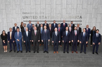 Un grupo de hombres con traje formal está sentado alrededor de una mesa en forma de U con las banderas de Guatemala y Estados Unidos