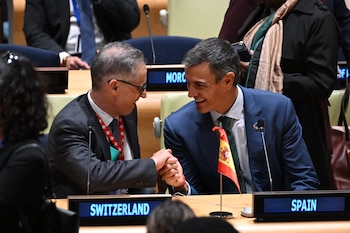 Pedro Sánchez y un representante oficial se dan la mano sentados ante escritorios con distintivos de Suiza y España