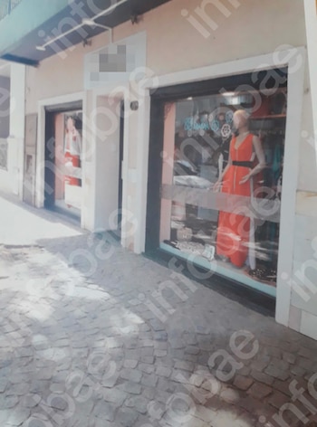 Vereda de adoquines frente a un edificio con locales comerciales. En una vidriera se observa un maniquí con vestido naranja y otra tienda borrosa