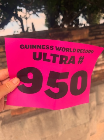 Una mano sostiene un papel rosa brillante con la inscripción en letras negras Guinness World Record Ultra 950 frente a un muro