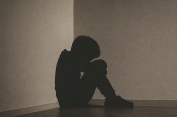 Sombra de un niño en la esquina de una pared, sentado en el suelo con la cabeza inclinada sobre sus rodillas.