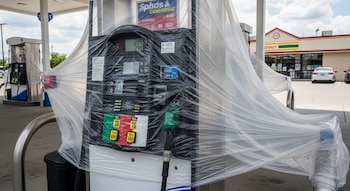 Vista de un surtidor de gasolina cubierto con plástico transparente en una estación de servicio de Estados Unidos, con otros surtidores y una tienda 7-Eleven en el fondo.