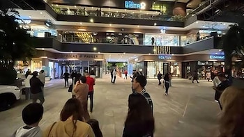 Personas de pie en la plaza central iluminada de un centro comercial de varios niveles con letreros y tiendas