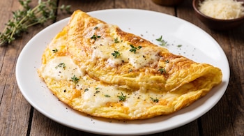 Una tortilla de huevo doblada con queso fundido, pimienta negra y hojas de tomillo en un plato blanco sobre madera.
