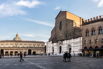 En el centro de la imagen se observa la Basílica de San Petronio, reconocida por su fachada inacabada de ladrillo y mármol. A la izquierda se encuentra el Palazzo del Podestà, edificio histórico con arcadas y una cúpula visible.