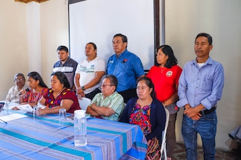 Un grupo de personas sentadas y de pie permanece junto a una mesa con un mantel a rayas durante una reunión