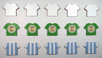 Una instalación de quince camisetas pequeñas: cinco blancas, cinco verdes con el texto 'Esto no es un juego', y cinco celestes y blancas