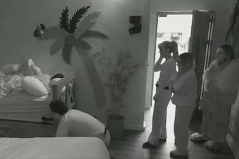 Imagen en blanco y negro de un hombre agachado en el suelo mientras tres mujeres lo observan de pie junto a la puerta abierta