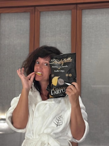 Griselda Siciliani, de cabelo preto e jaqueta branca, come batatas fritas trufadas em um saco de marca preta