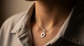 Primer plano del cuello y hombro de una persona vestida con una camisa, luciendo un colgante plateado con la forma de la Estrella de David.