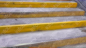 Vista de una escalera de estación de tren con peldaños de concreto y franjas amarillas antideslizantes, mostrando desgaste y algunas manchas